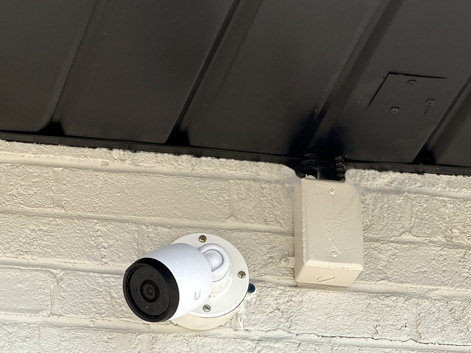 Camera mounted on painted brick under a metal soffit